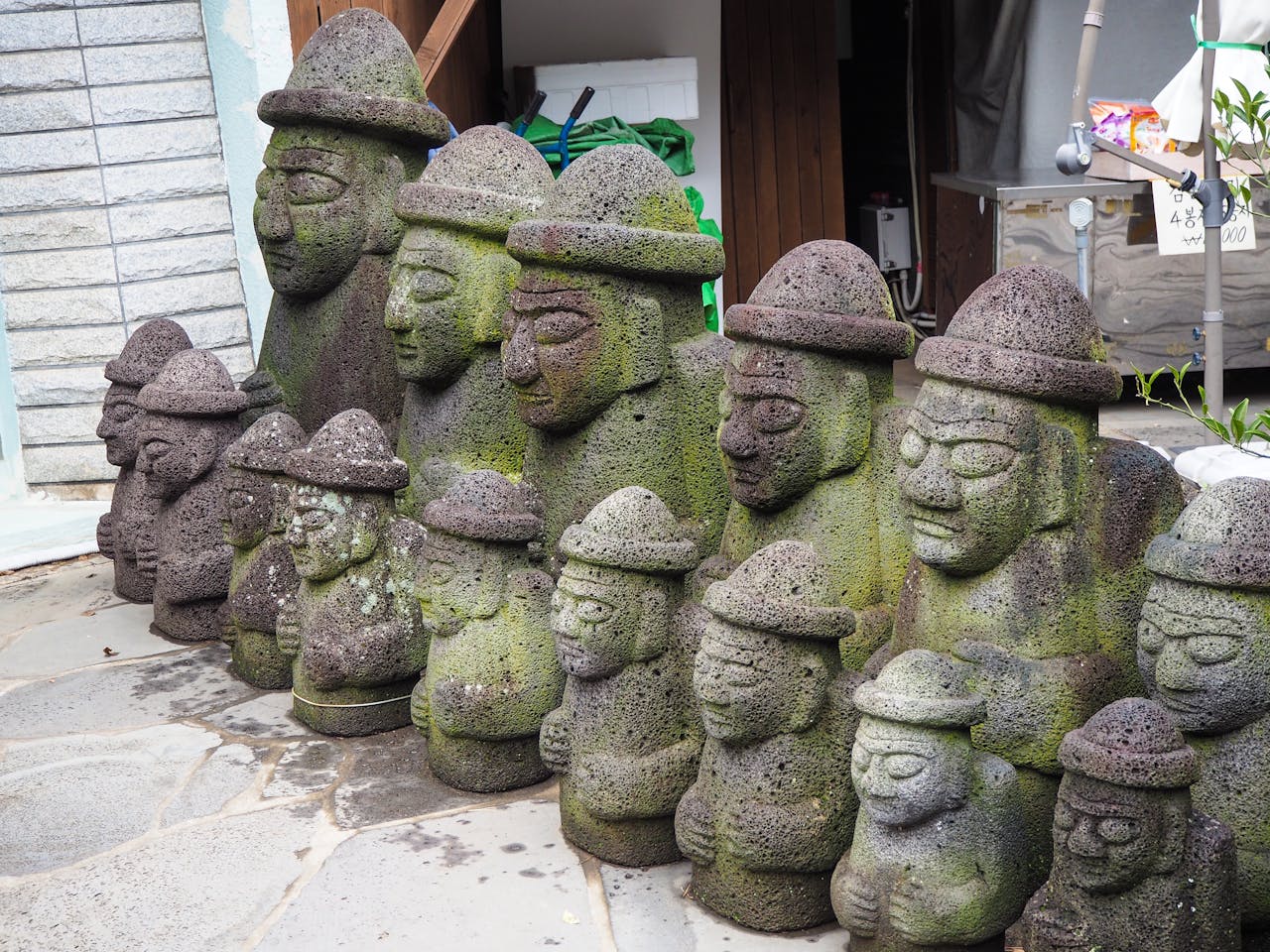 Row of moss-covered Dol Hareubang statues, stone guardians from Jeju Island, outdoors.