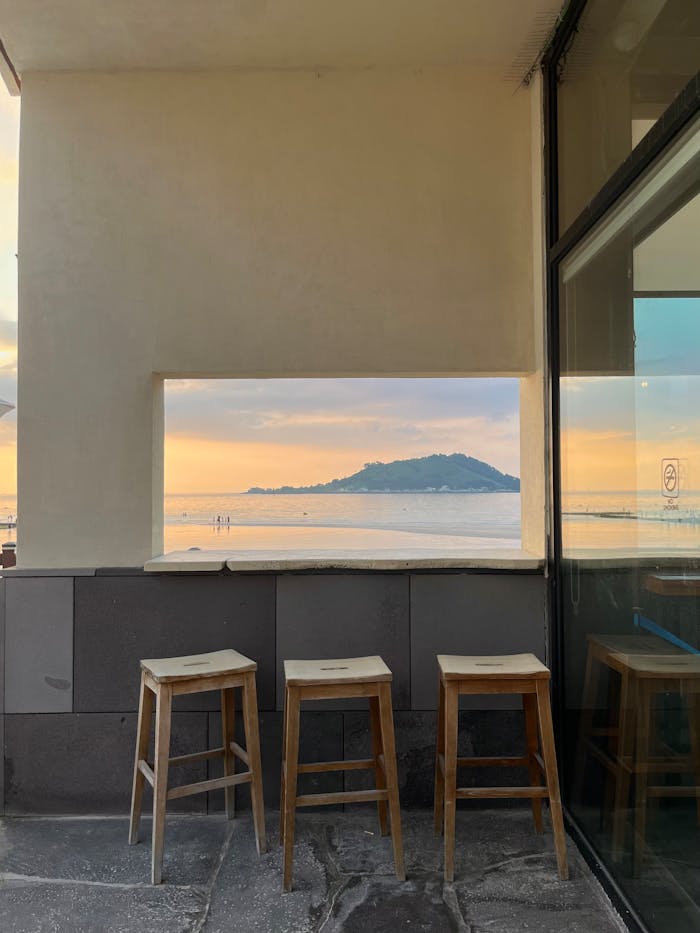 Wooden stools in a minimalist cafe overlooking the ocean and mountains at sunset in Jeju, South Korea.